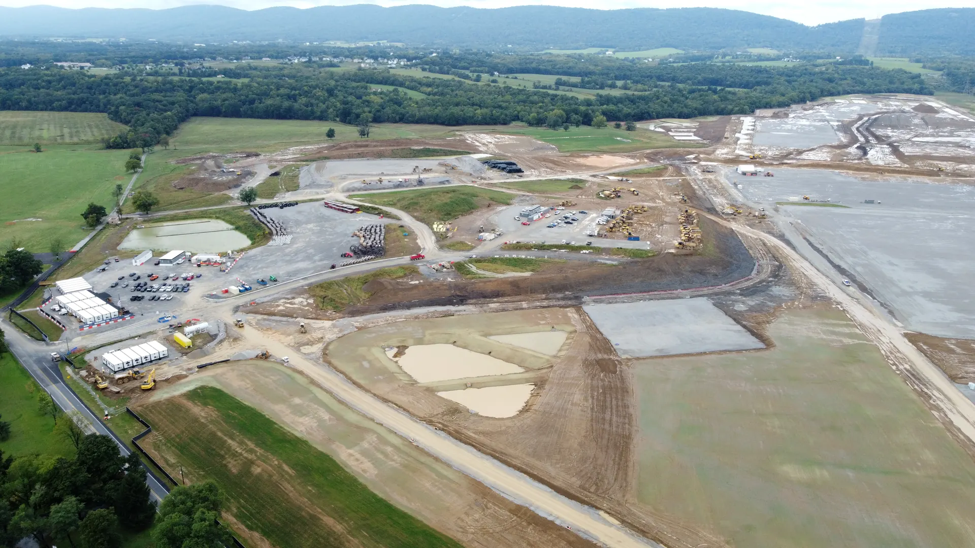 An aerial view of the PAX-1 site on September 22, 2026: the fields graded to bare earth, with gravel pads, stormwater basins and construction trailers, and farmland and the mountain beyond.